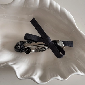 Close-up of gray fabric bow hair clip with decorative heart and smile bead chain detail