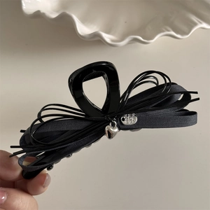 Detail of black ribbon hair clip featuring silver heart charm and metal logo tag