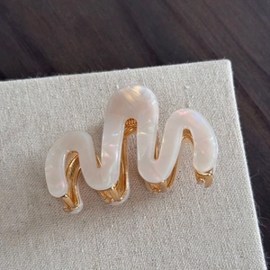 Détail d'une pince à cheveux ondulée en acétate blanc nacré avec base en métal doré