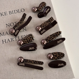 Close-up of leopard print hair clips with brown pearls and golden lettering detail