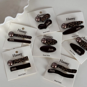 Leopard print hair clip set with champagne pearls and gold lettering on white surface
