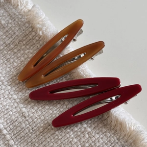 Détail de quatre barrettes à cheveux creuses en acétate rouge foncé et brun ambre