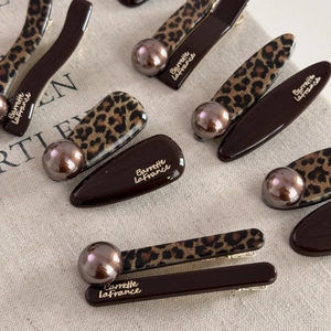 Close-up of leopard print hair clips with champagne pearl details and metallic text