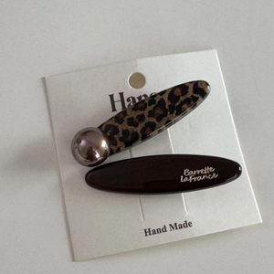 Detailed view of leopard print hair clip with gold logo lettering on card