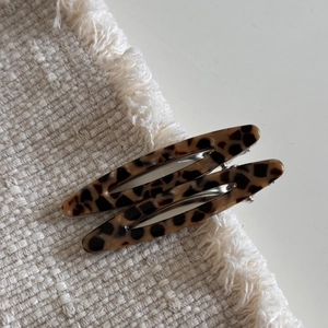 Détail de deux pinces à cheveux écaillées évidées sur un fond de tissu beige texturé