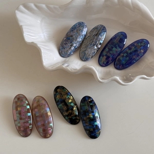 Close-up of eight handmade mosaic shell hair clips in assorted colors on a ceramic tray