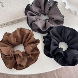 Three-pack oversized fabric hair scrunchies in brown, gray, and black on a white table