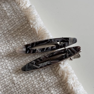 Détail de deux barrettes en acétate avec motif marbré gris sur tissu en lin