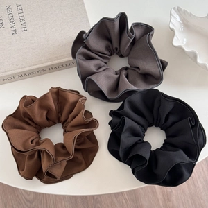 Detail of three solid color scrunchies in grey, brown and black with delicate ruffled edges