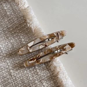 Vue détaillée de barrettes en acétate avec texture marbrée ambre sur fond en tissu beige