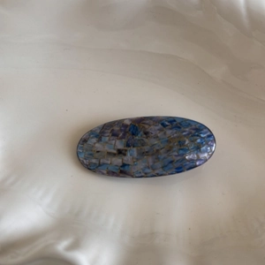 Detail of oval hair clip with blue and purple iridescent shell mosaic and gold metal edges