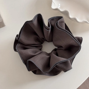 Close-up of dark grey large scrunchie made of textured fabric on a white ceramic plate