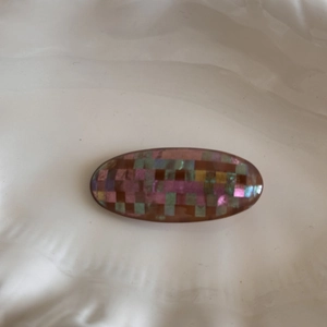 Detailed macro view of an oval hair clip with iridescent shell mosaic tiles and amber base
