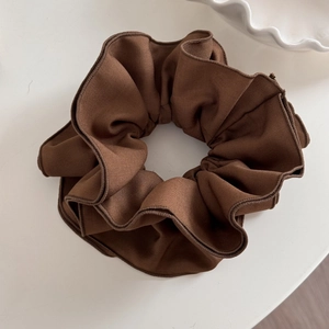 Macro detail of brown textured fabric scrunchie with rich pleated layers for hair