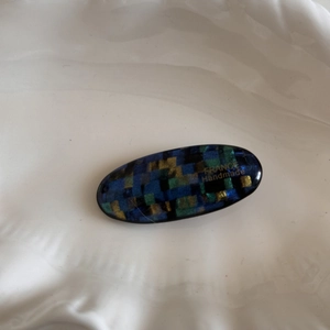 Close-up of oval hair clip with blue and green mosaic glitter pattern and France Handmade text