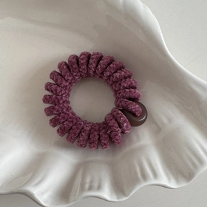 Dettaglio dell'elastico a spirale in velluto di ciniglia viola con bottone decorativo marrone