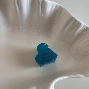 Detailed shot of a blue heart hair claw clip on a white shell plate with gold lettering