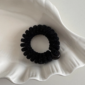 Dettaglio dell'elastico per capelli a spirale in ciniglia nera con perla su vassoio