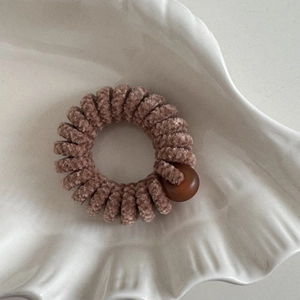 Dettaglio di un elastico a spirale in ciniglia marrone con una perla liscia su vassoio bianco