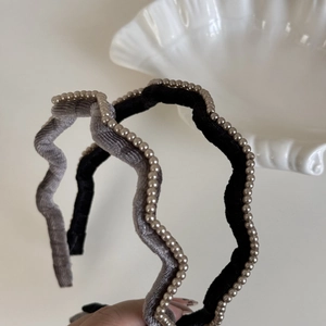Close-up of wavy velvet headbands with pearl trim in grey and black colors