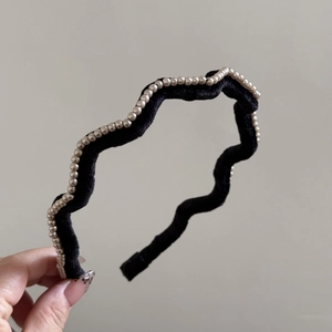 Detailed close-up showing the wavy black velvet texture and gold pearl edges of the headband