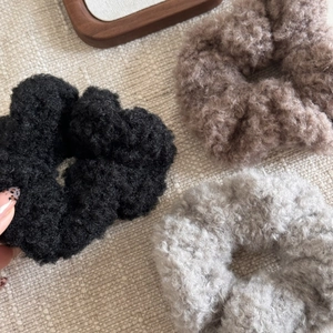 Détail de chouchous en peluche noire, marron et grise sur un fond textile tissé