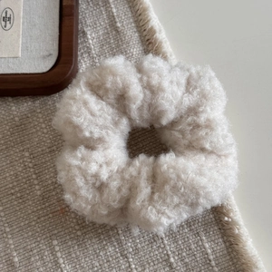 Gros plan d'un chouchou en peluche beige à texture laine d'agneau sur fond de lin