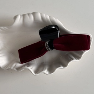 Macro shot of wine red velvet bow hair clip with grey rhinestones on a white shell tray
