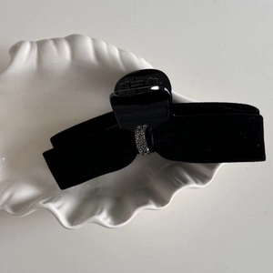 Close-up of velvet black bow hair clip with grey rhinestones on a white shell tray