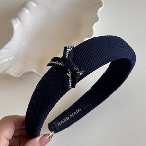 Détail du bandeau en tissu côtelé bleu marine avec un nœud décoratif et étiquette interne
