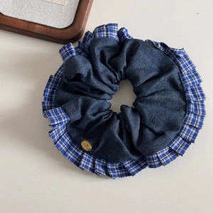 Close-up of blue plaid scrunchie with denim texture and gold metal brand emblem
