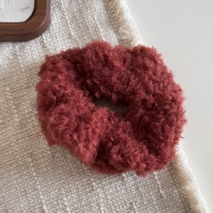 Gros plan sur chouchou en peluche rouge rouille avec texture douce sur tissu en lin