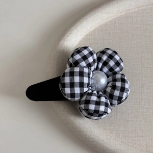 Detail of checkered fabric flower hair clip with a center pearl and matte black base