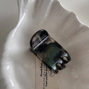 Detail of grey marble acetate hair claw clip with gold lettering on a white shell tray