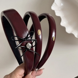 Close-up of burgundy leather headbands with bow, silver heart charm, and golden Love tags