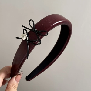 Detail of burgundy faux leather headband with black bows and silver heart charm