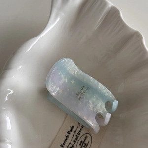 Close-up of marble acetate hair claw clip in pale blue and violet on a white shell tray