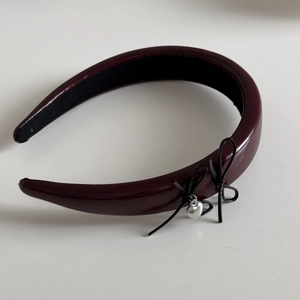 Close-up of burgundy faux leather headband with black bows and a silver heart pendant