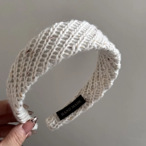 Close-up of a white hand-knitted headband with a 'HAND MADE' label detail