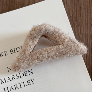 Gros plan sur une pince à cheveux en peluche beige sur un livre et surface boisée