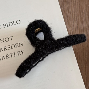 Macro view of black fuzzy plush shark hair claw clip with golden metal spring details