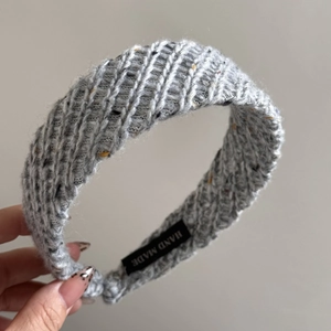 Detailed close-up of handmade grey knit headband with woven texture and satin label