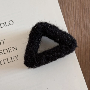 Detail of triangular black plush hair claw with shimmering silver threads on book background