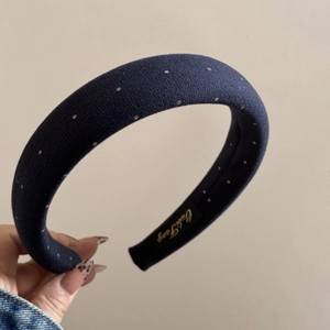 Close-up of a navy blue padded headband with small white polka dots and golden logo tag