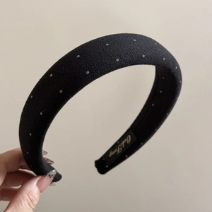 Detailed close-up of a black padded headband with white polka dots and a brand label