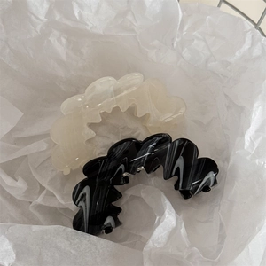 Detail of wavy acetate hair clips in creamy white and black marble texture