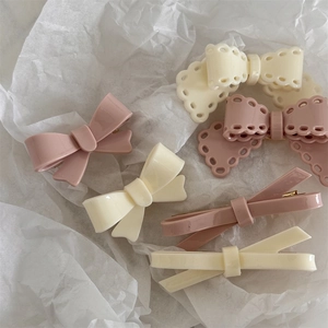 Detailed view of cream and pink bow hair clips with glossy finish on textured paper