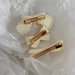 Detail view of cream pink bow hair clips with gold metal grips on textured background