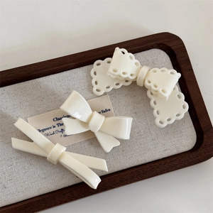 Three-piece set of cream white bow hair clips on a premium walnut display tray