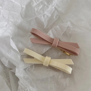 Close-up of pink and cream bow hair clips with gold metal duckbill clips on white background